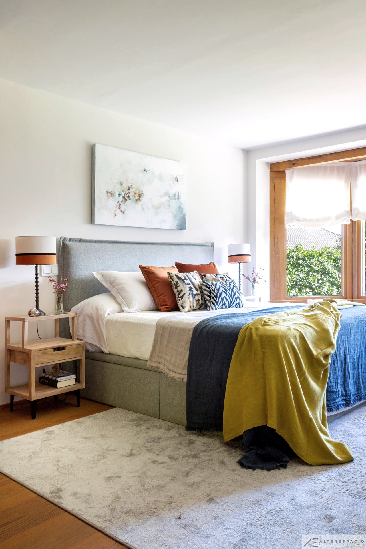 Dormitorio principal con cabecero tapizado y textiles en azul y mostaza